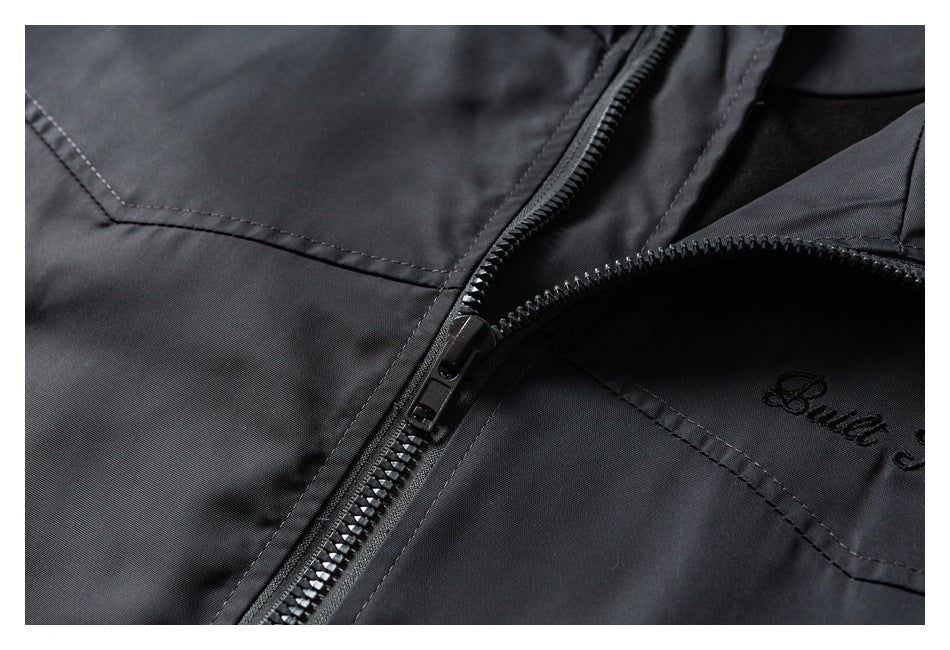 Close-up of a black jacket with a diagonal zipper, stitched panels, and partial black script embroidery.