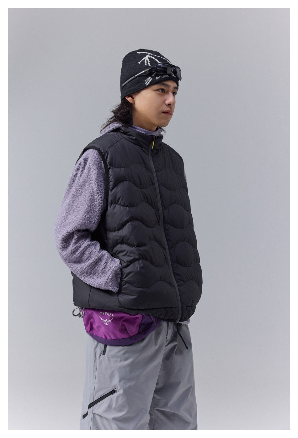 Model wearing a black wave-quilted vest over a lavender fleece, shown from the side.