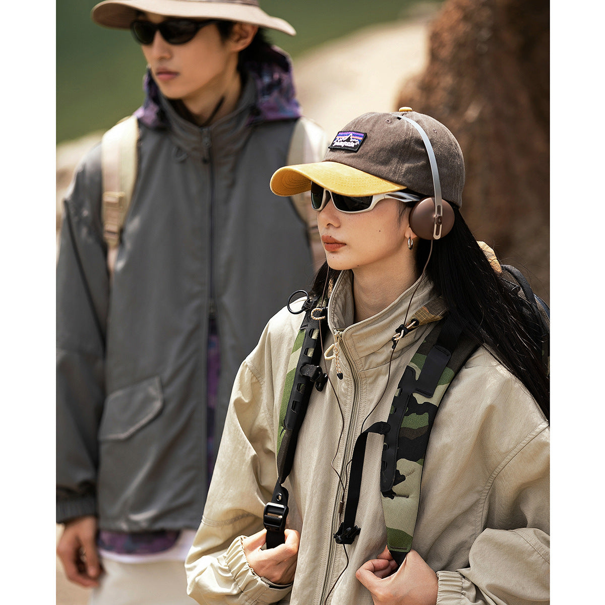 Woman wearing a beige zip-front outdoor jacket with a high collar, beside a man in a charcoal jacket.
