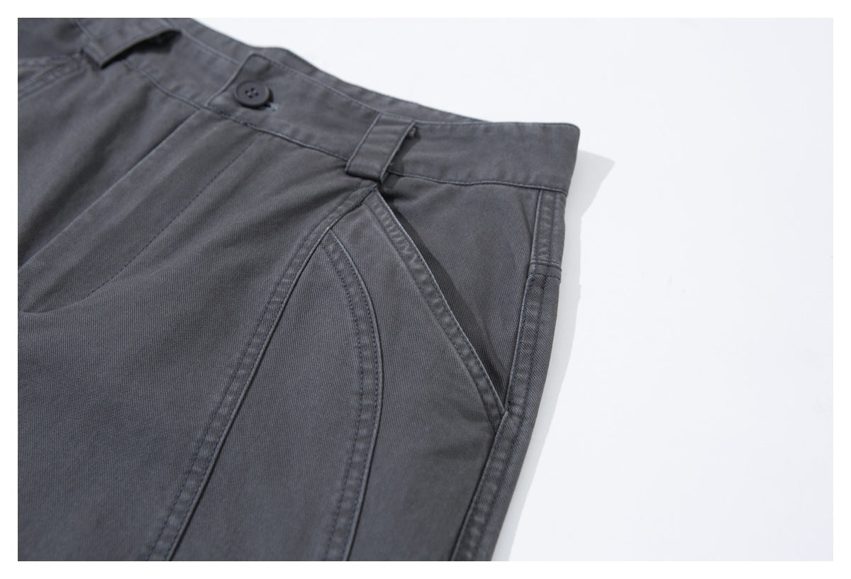 Close-up of charcoal trousers showing the waistband button, belt loop, and angled pocket stitching.