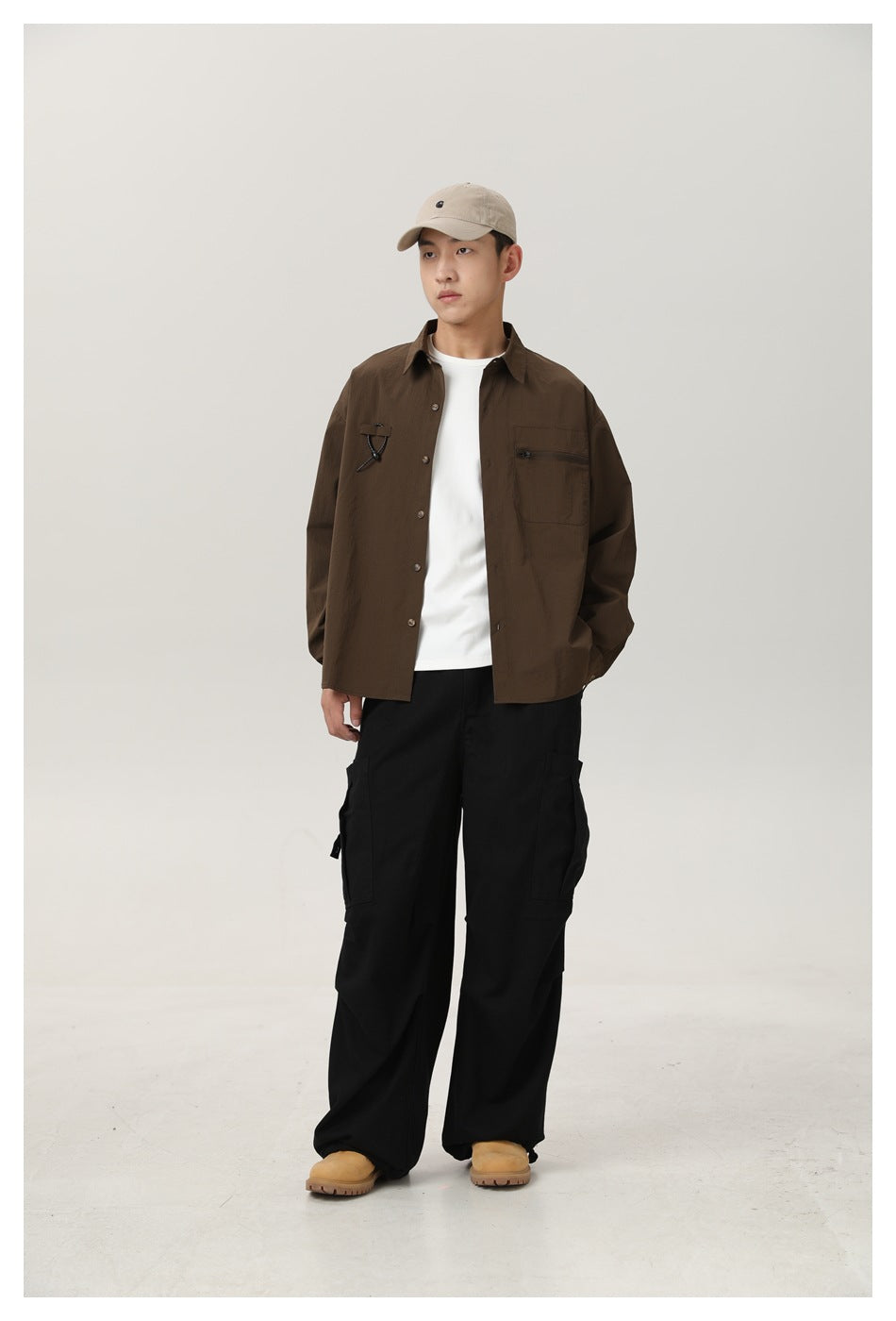 Model wearing open brown button-up shirt over a white tee with black cargo pants, cap and tan boots