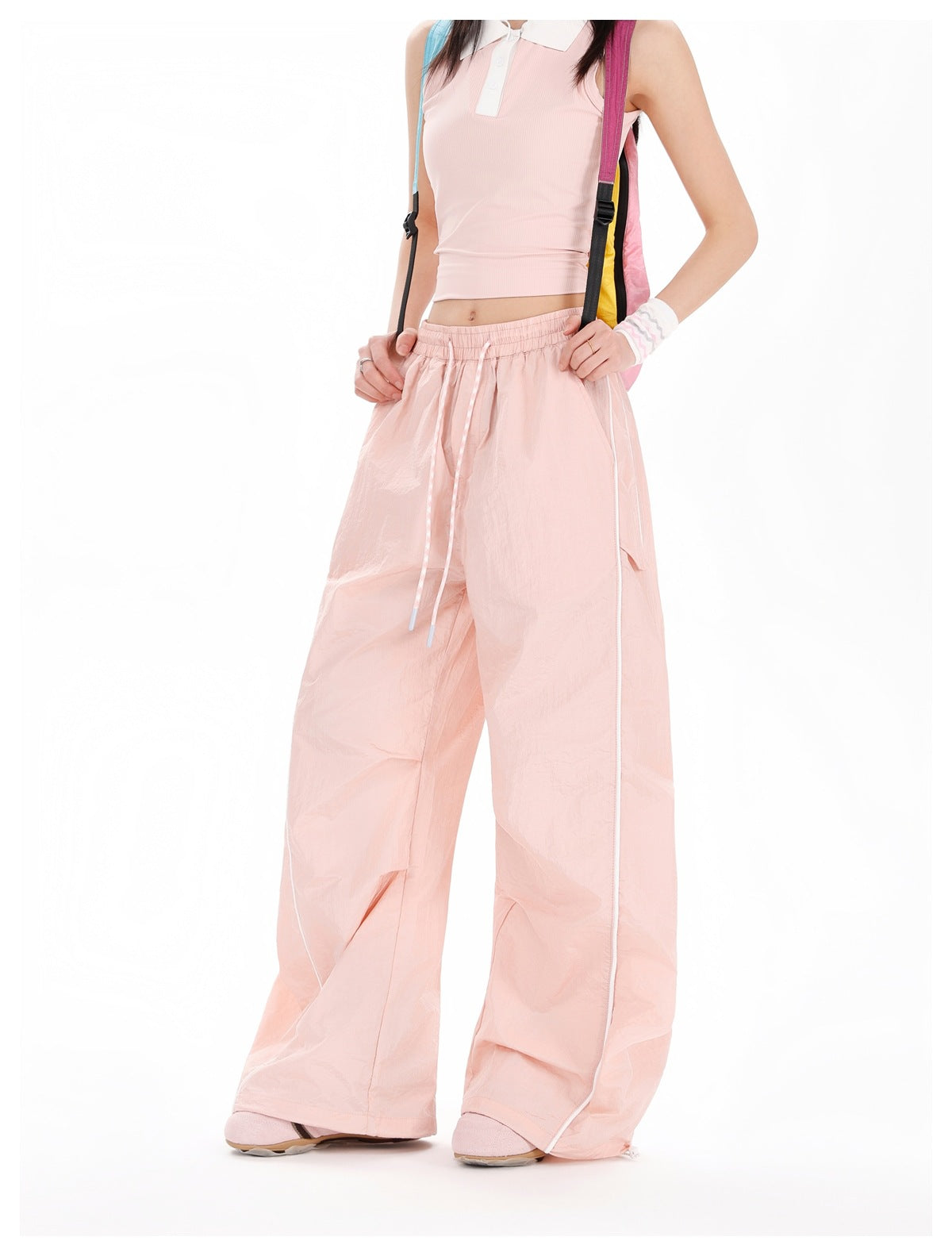 Cropped front view of a model wearing pale pink wide-leg drawstring pants with white piping and a sleeveless collared top.