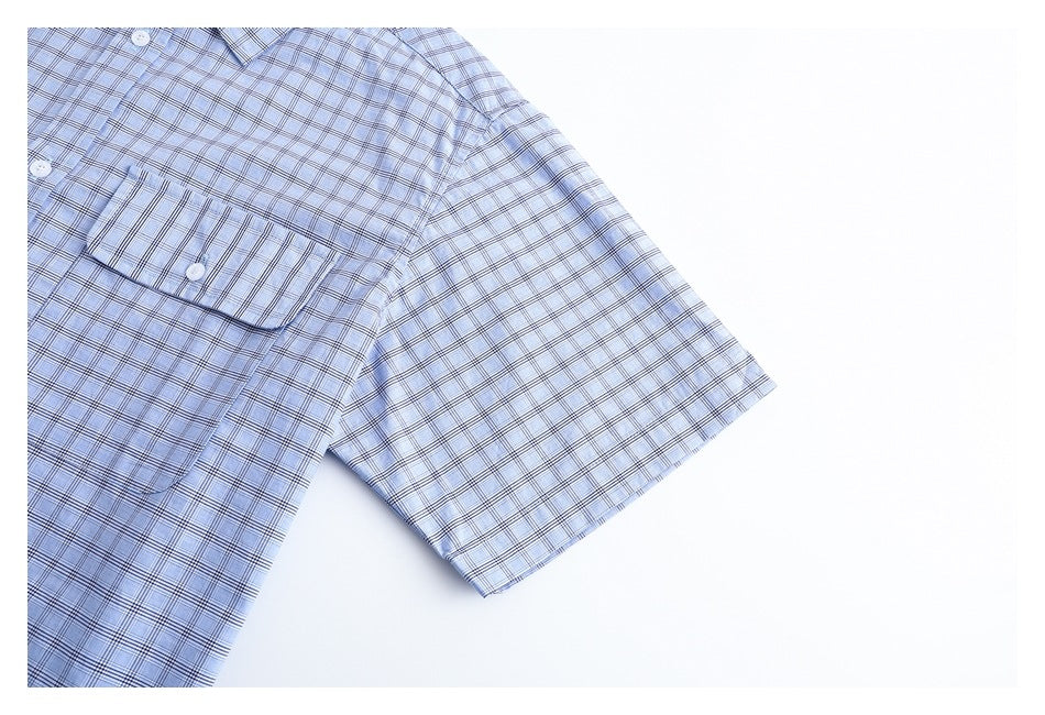 Close-up of a short sleeve and chest pocket on a light blue plaid shirt.
