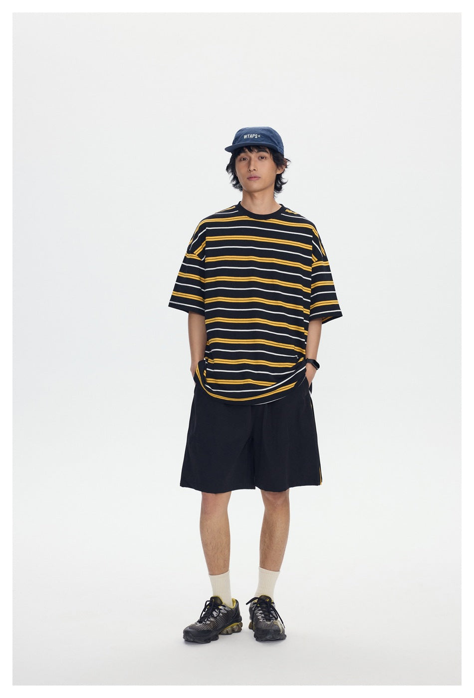 Full-length front view of a model wearing a black oversized T-shirt with yellow and white stripes and black shorts.
