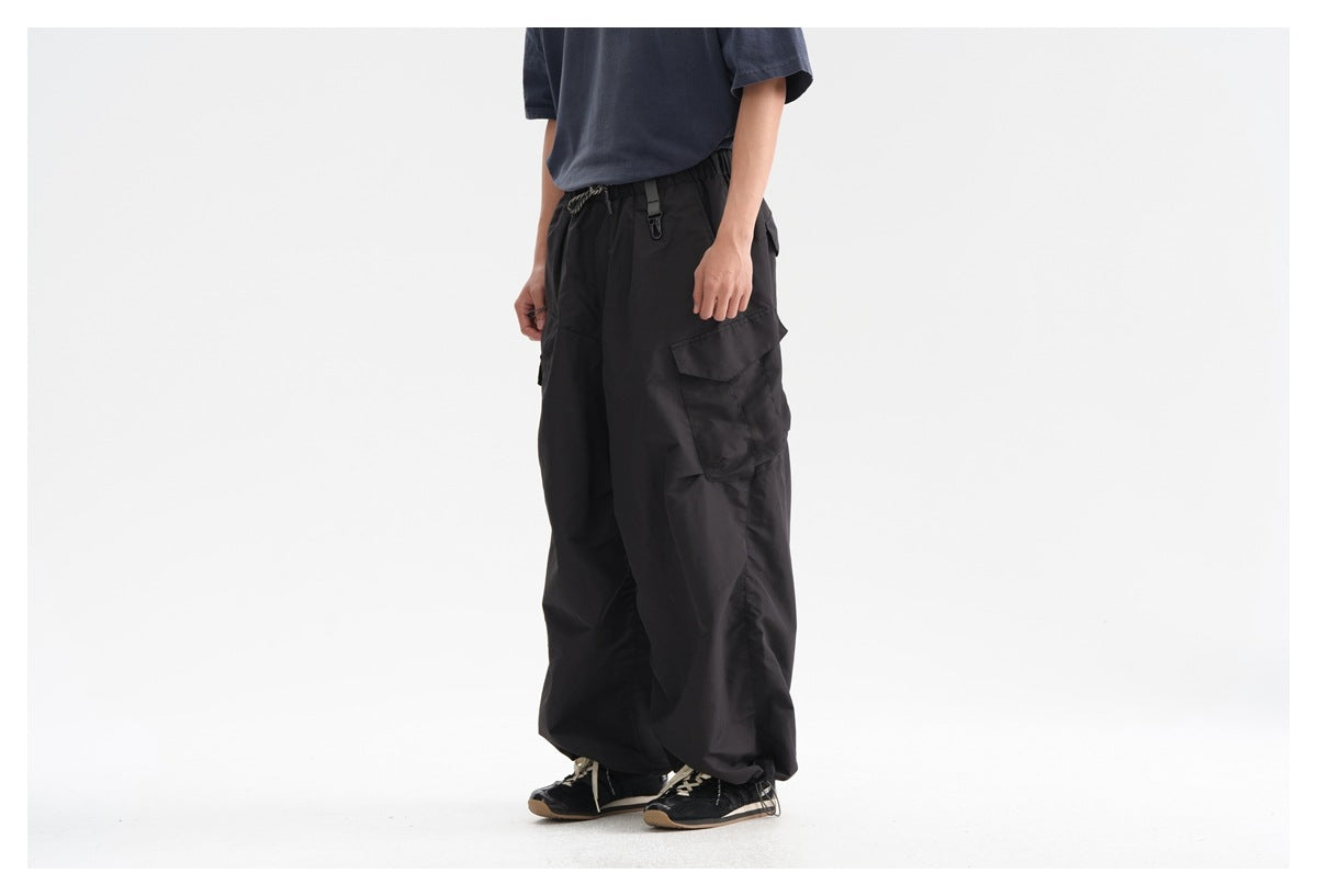 Front three-quarter view of a model wearing loose black cargo pants with large flap pockets and an elastic drawstring waist.