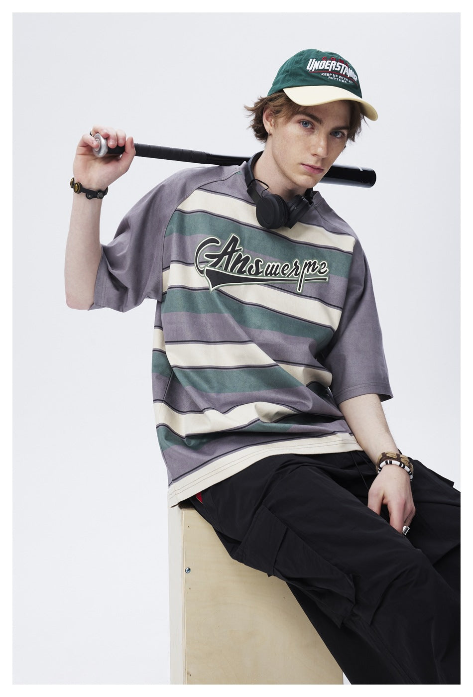 Model wearing an oversized gray-purple, cream and teal striped graphic T-shirt with black trousers.