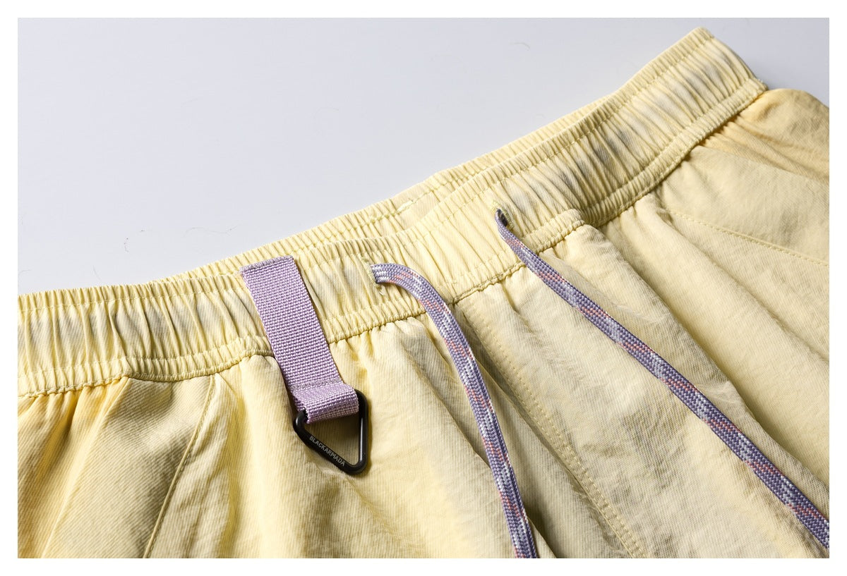 Close-up of pale yellow shorts showing the elastic waistband, lavender drawcords, and a small webbing loop.