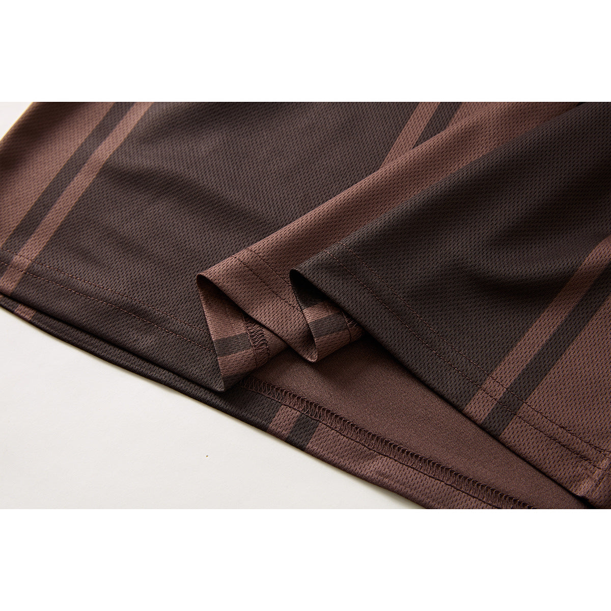 Close-up of the dark brown striped polo shirt’s hem and sleeve seam stitching.