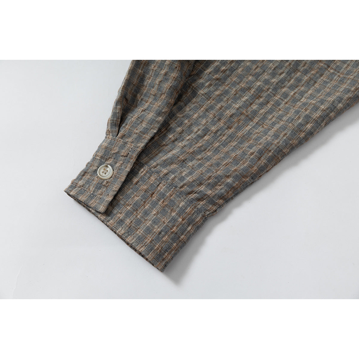 Close-up of a gray-brown plaid shirt sleeve cuff with a light button.