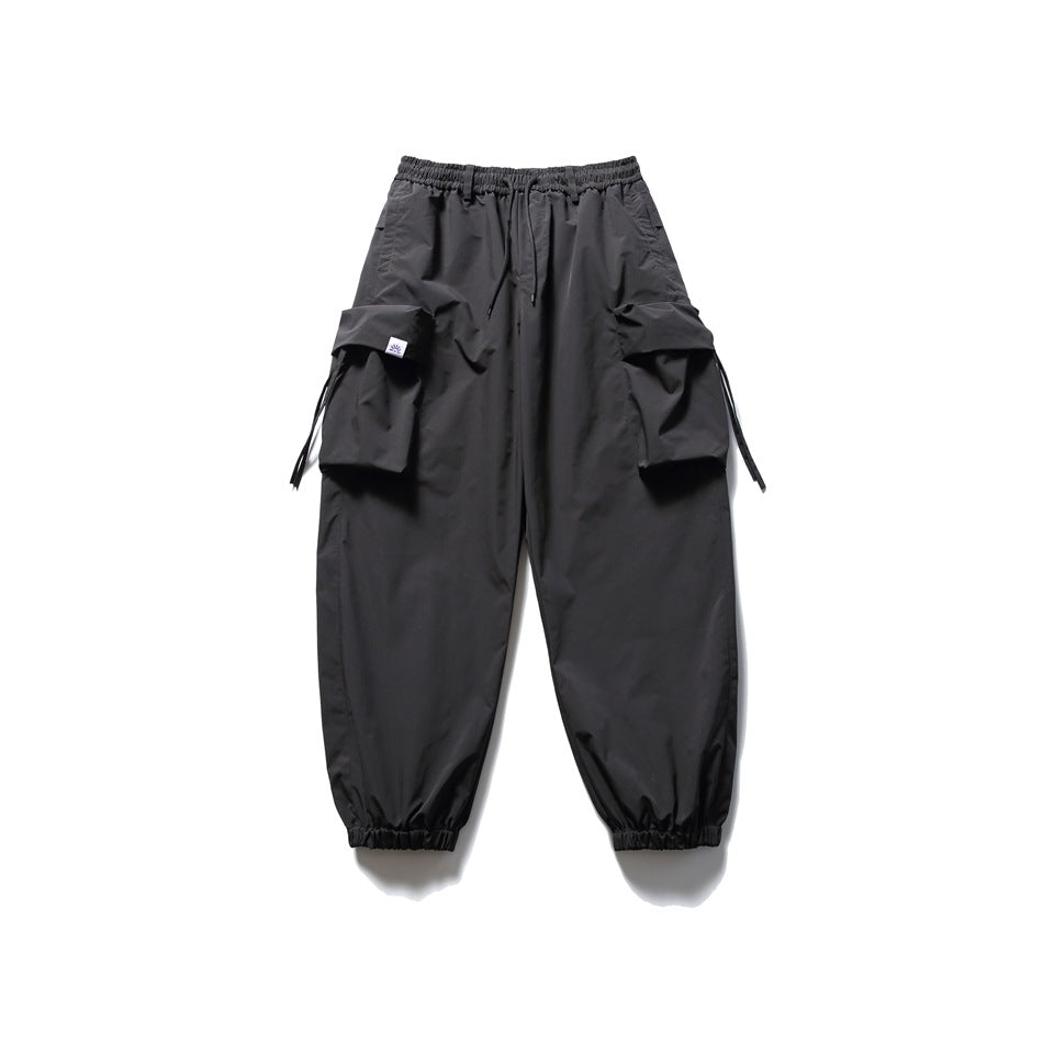 Black cargo jogger pants with elastic drawstring waist, large flap pockets and gathered cuffs, flat lay on white