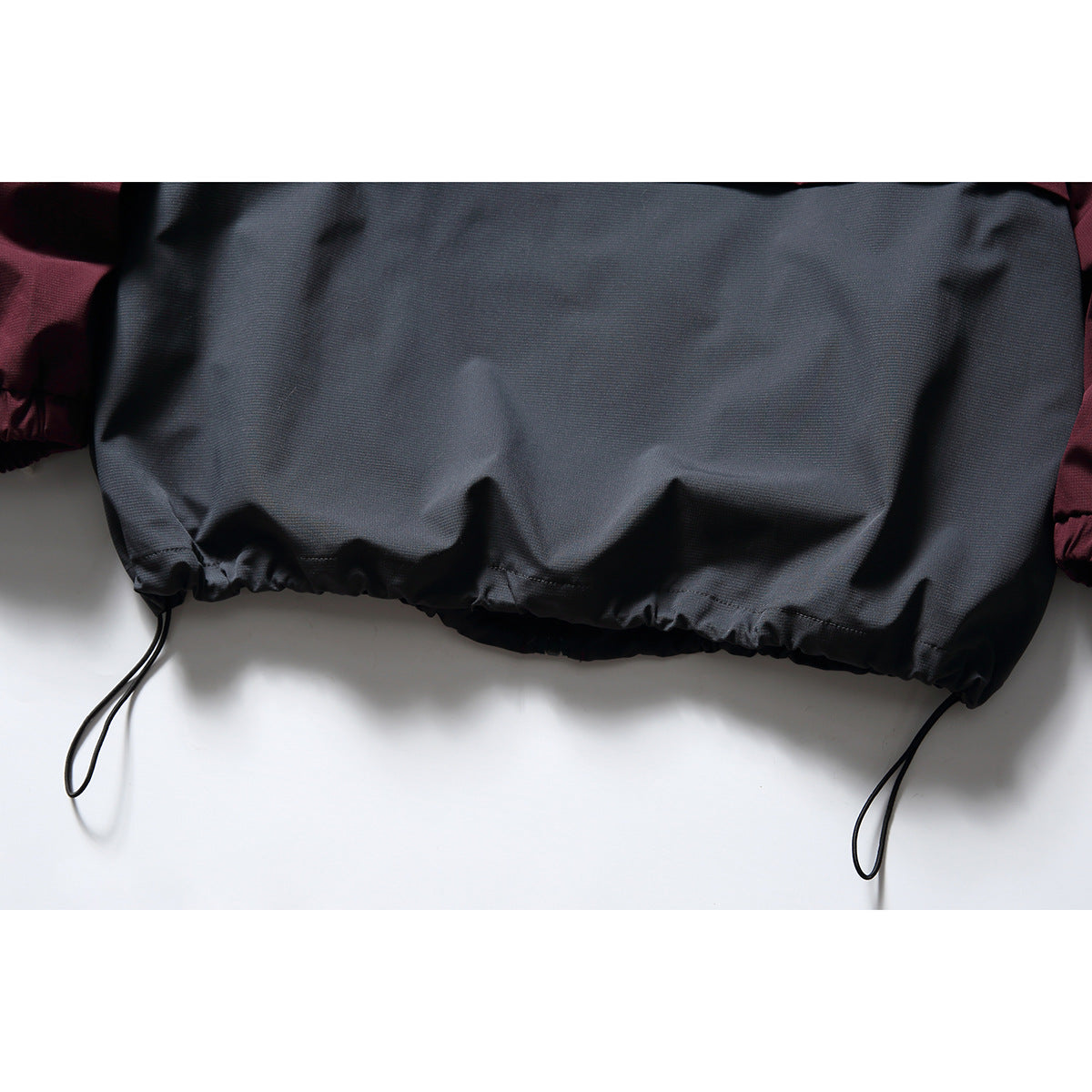 Close-up of the charcoal jacket hem with two dangling adjustment cords and burgundy fabric at the sides.