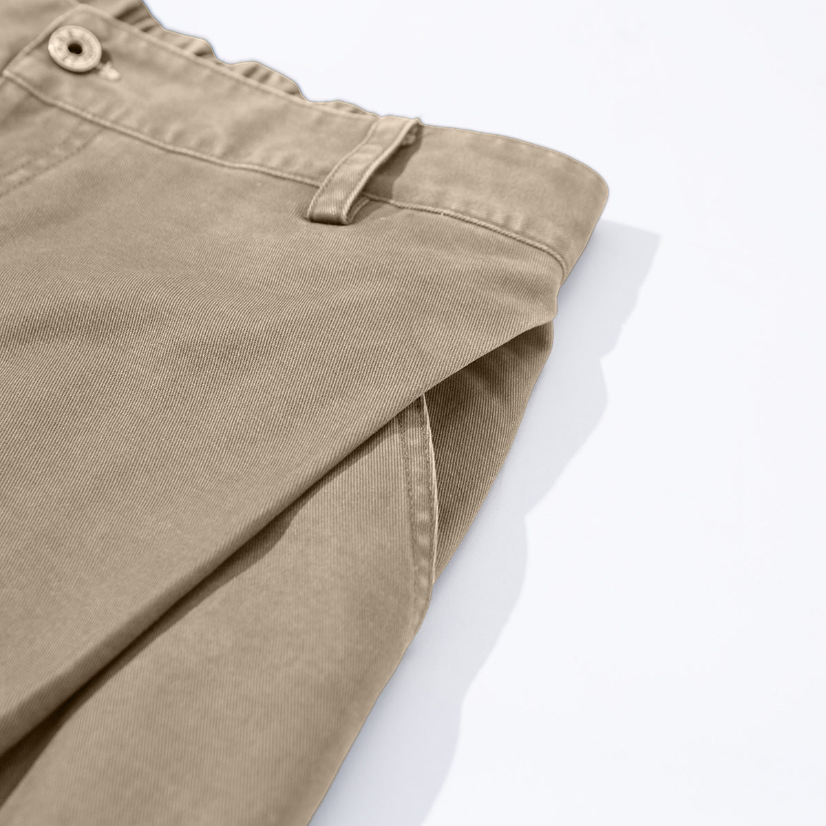 Angled close-up of folded taupe trousers showing the buttoned waistband, belt loop, and side seam.