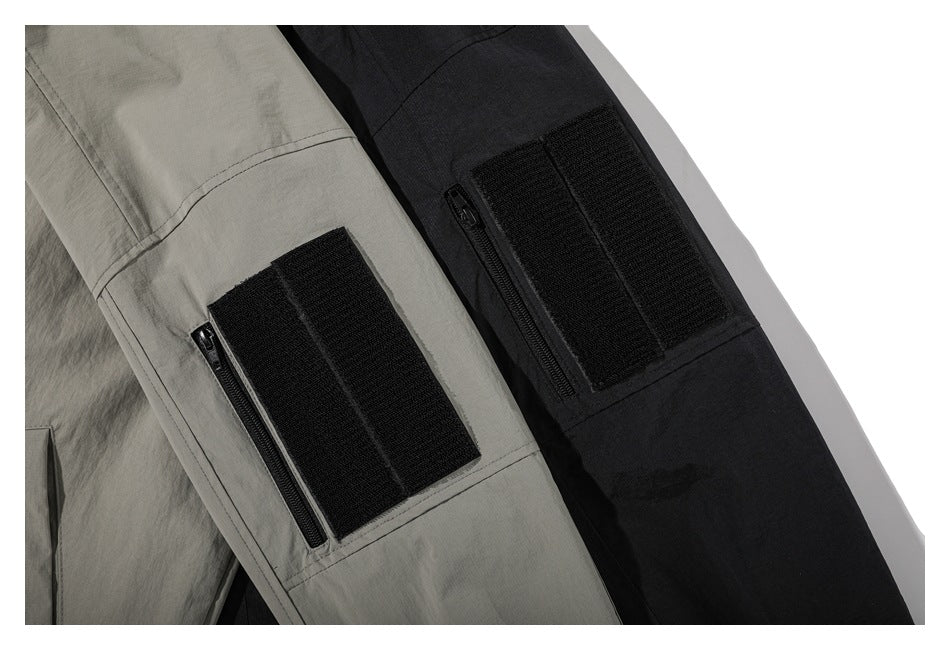 Close-up of gray and black jacket sleeves, each with a black zip pocket and rectangular hook-and-loop patch panel.