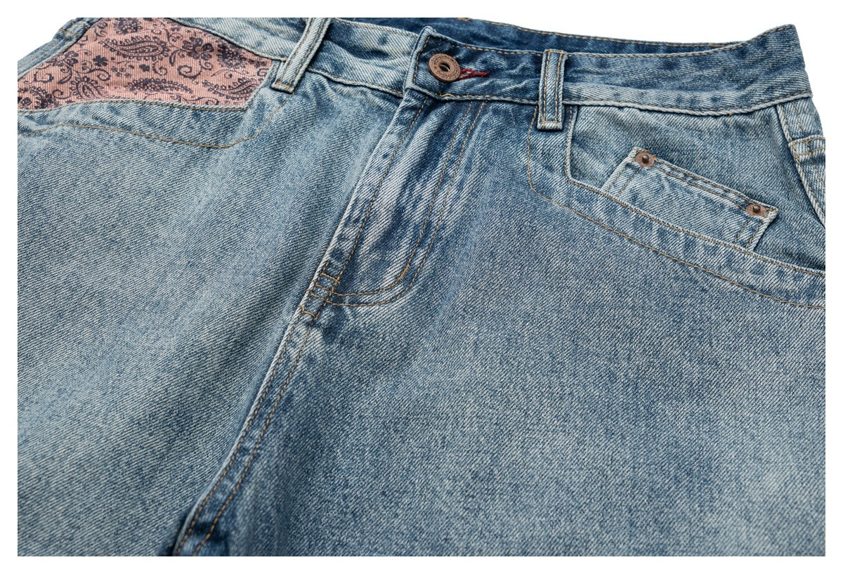 Close-up of light blue jeans showing the buttoned waist, front pocket stitching, and pink paisley pocket lining.