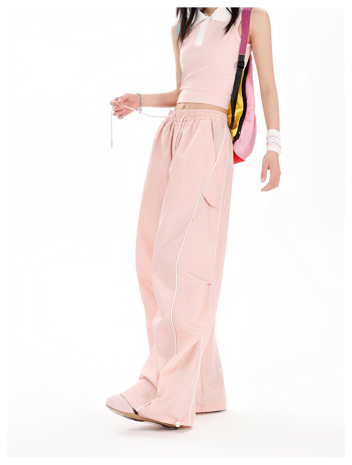 Cropped side view of a model wearing pale pink wide-leg pants with a drawstring waist, flap pockets and white piping.