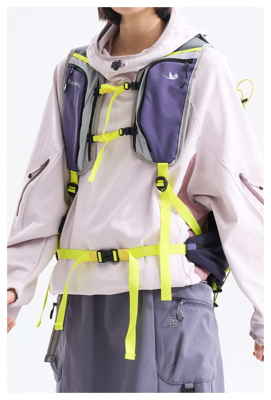 Close-up of a model wearing a pale hooded jacket and a purple-gray chest pack with neon yellow straps.