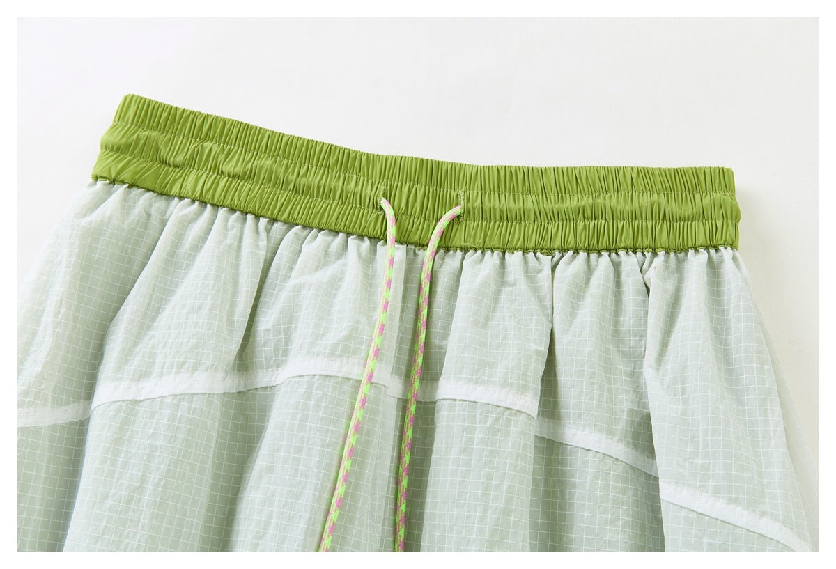 Close-up of a pale green grid-patterned skirt with a wide lime-green elastic waistband and pink-and-green drawcord.