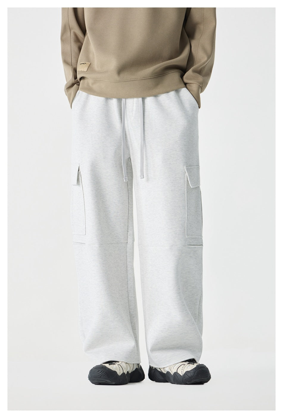 Model wearing gray wide-leg cargo pants with a tan sweatshirt and chunky sneakers, front view with hands in pockets