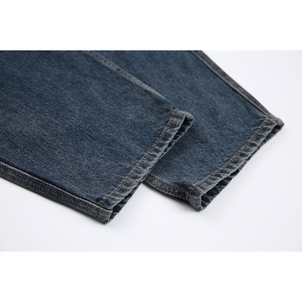 Close-up of the stitched hems on dark blue washed jeans, laid flat against a white background.