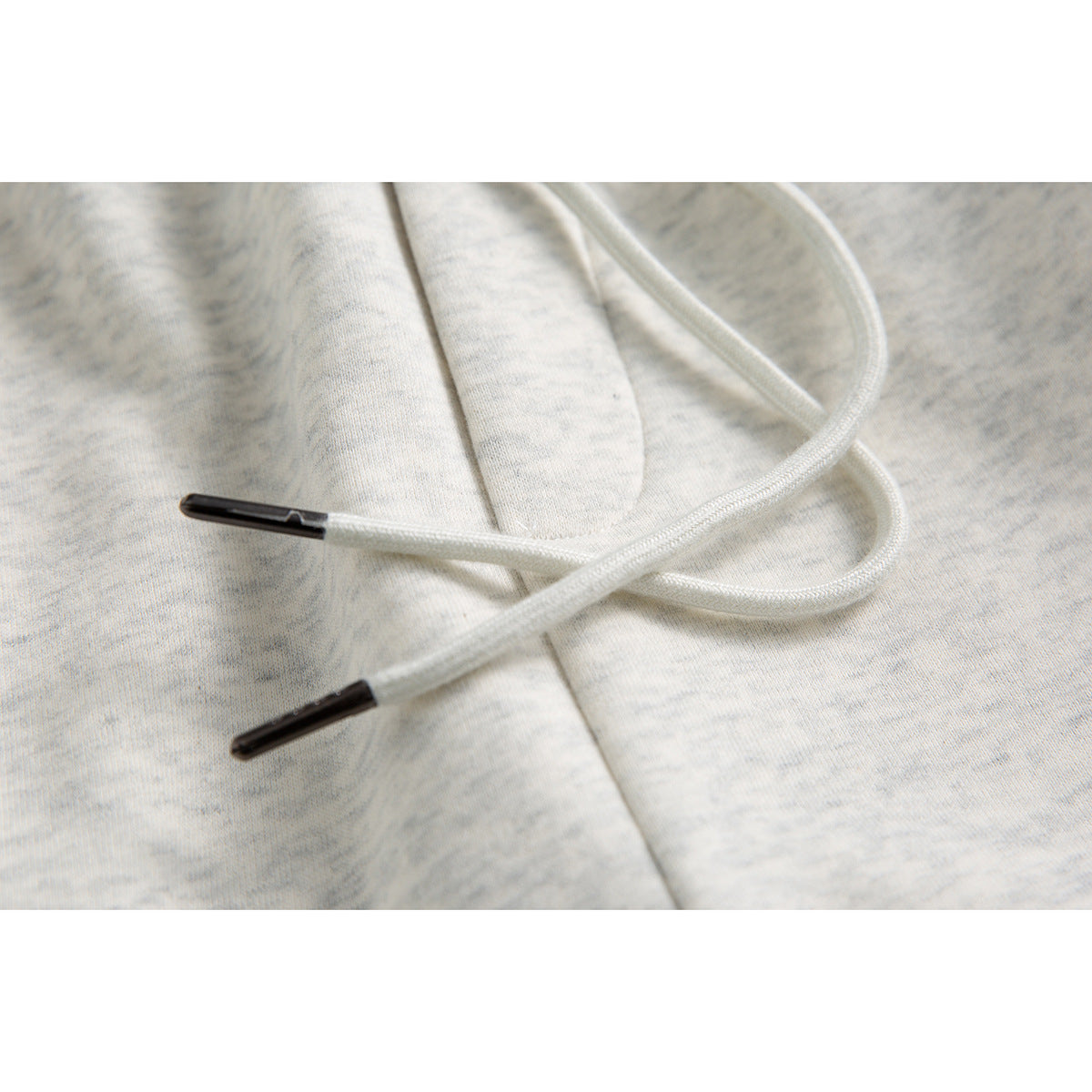 Close-up of white drawstrings with black tips lying across light gray heather sweatpants.