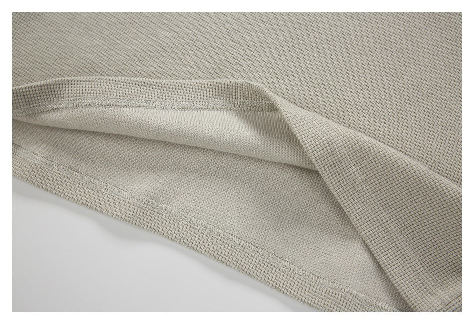 Close-up of a light beige-gray garment's folded hem, showing the inner side and stitching.