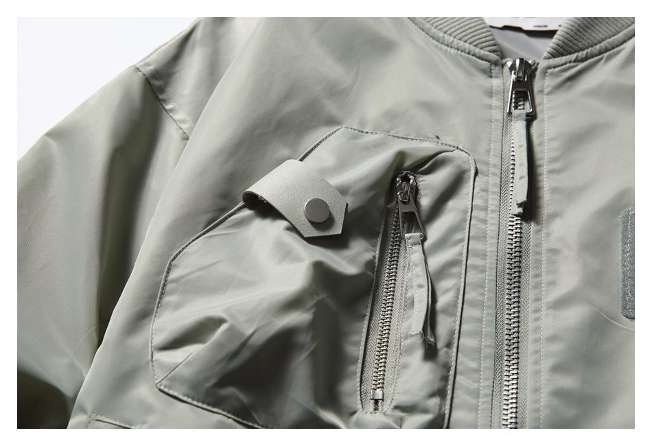 Close-up of a pale gray-green jacket chest pocket with a zippered compartment and snap tab.
