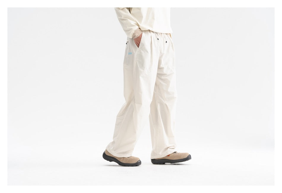 Front three-quarter view of a model wearing loose cream pants with an elastic waist and roomy pockets.