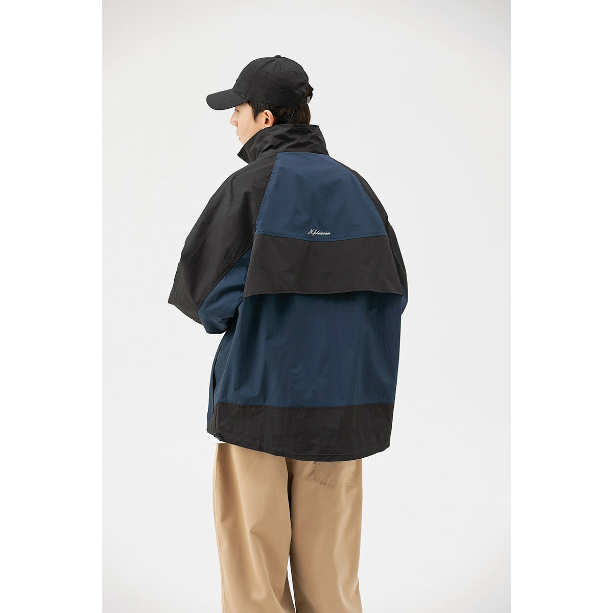 Back view of a model wearing a navy and black color-block jacket with a large back vent panel.