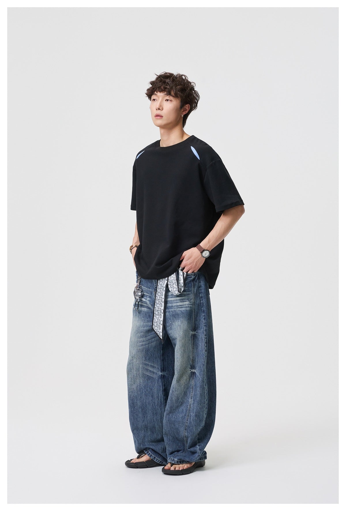 Full-length model wearing a black oversized T-shirt with light-blue shoulder accents and wide-leg blue jeans.