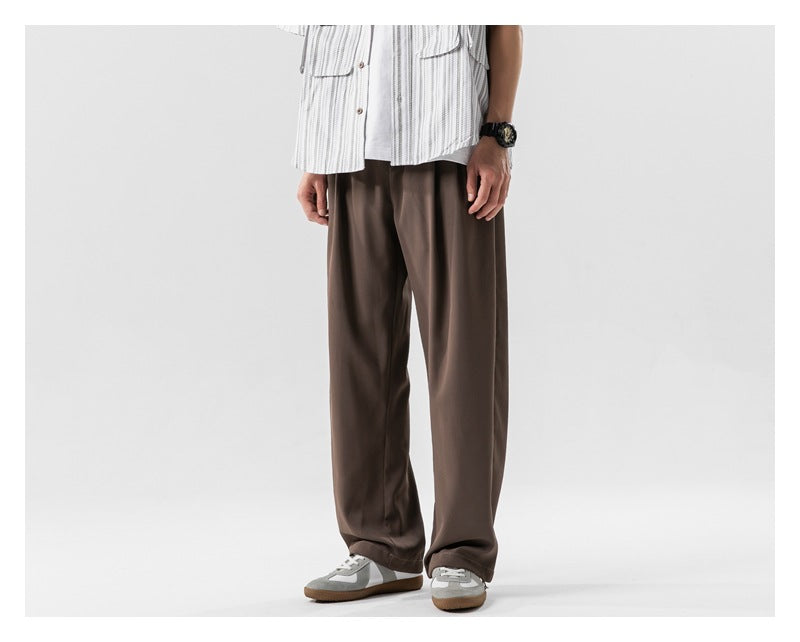 A person models loose brown trousers with wide straight legs and sneakers, shown from the front.