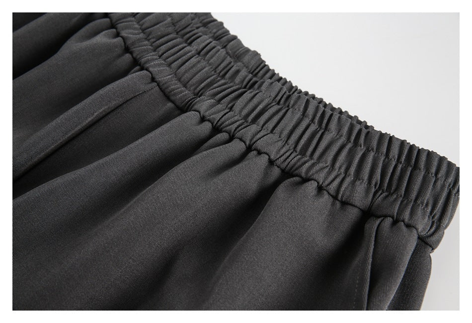 Close-up showing the gathered waistband stitching and pleats on charcoal gray pants.