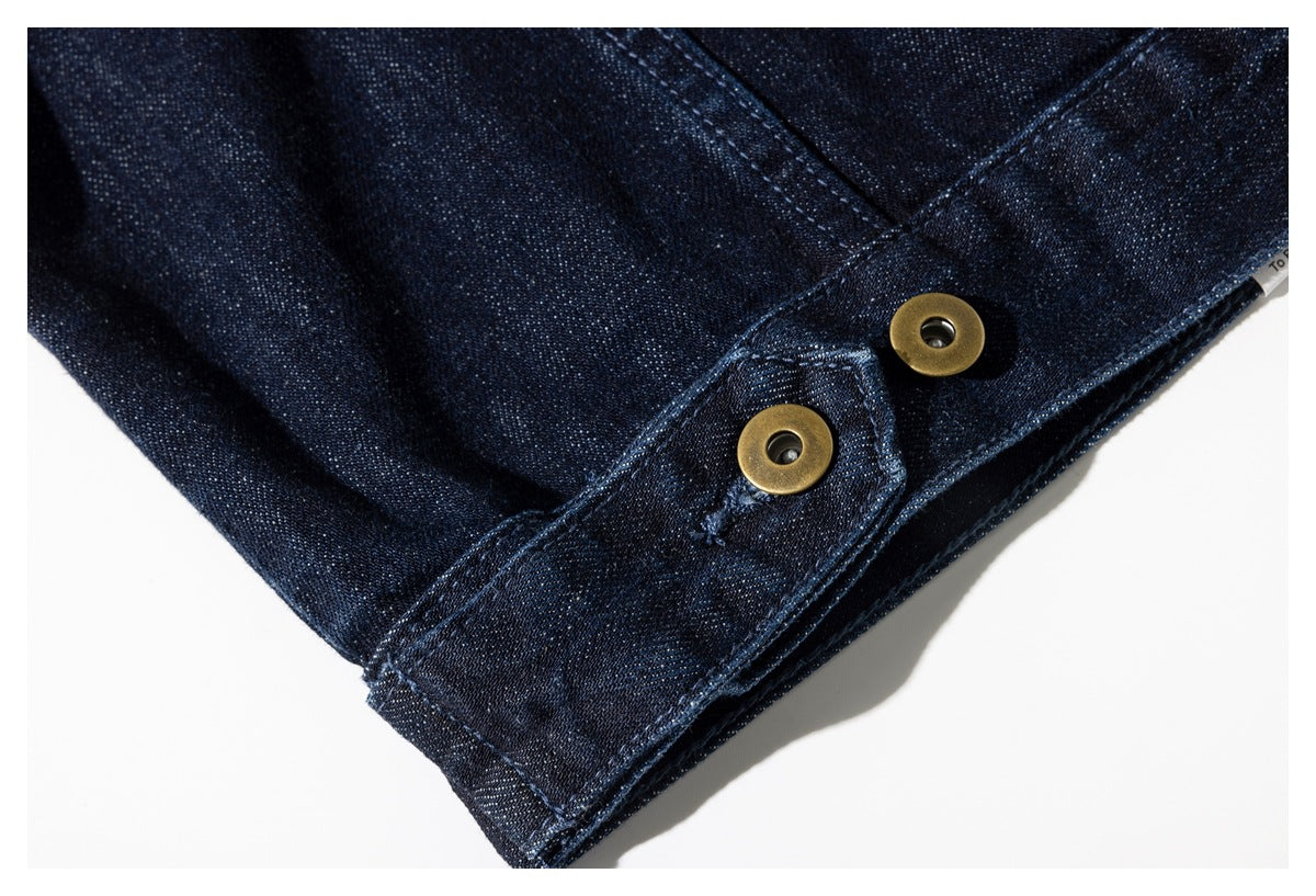 Close-up of dark indigo denim with two round brass-colored snap fasteners along an edge.