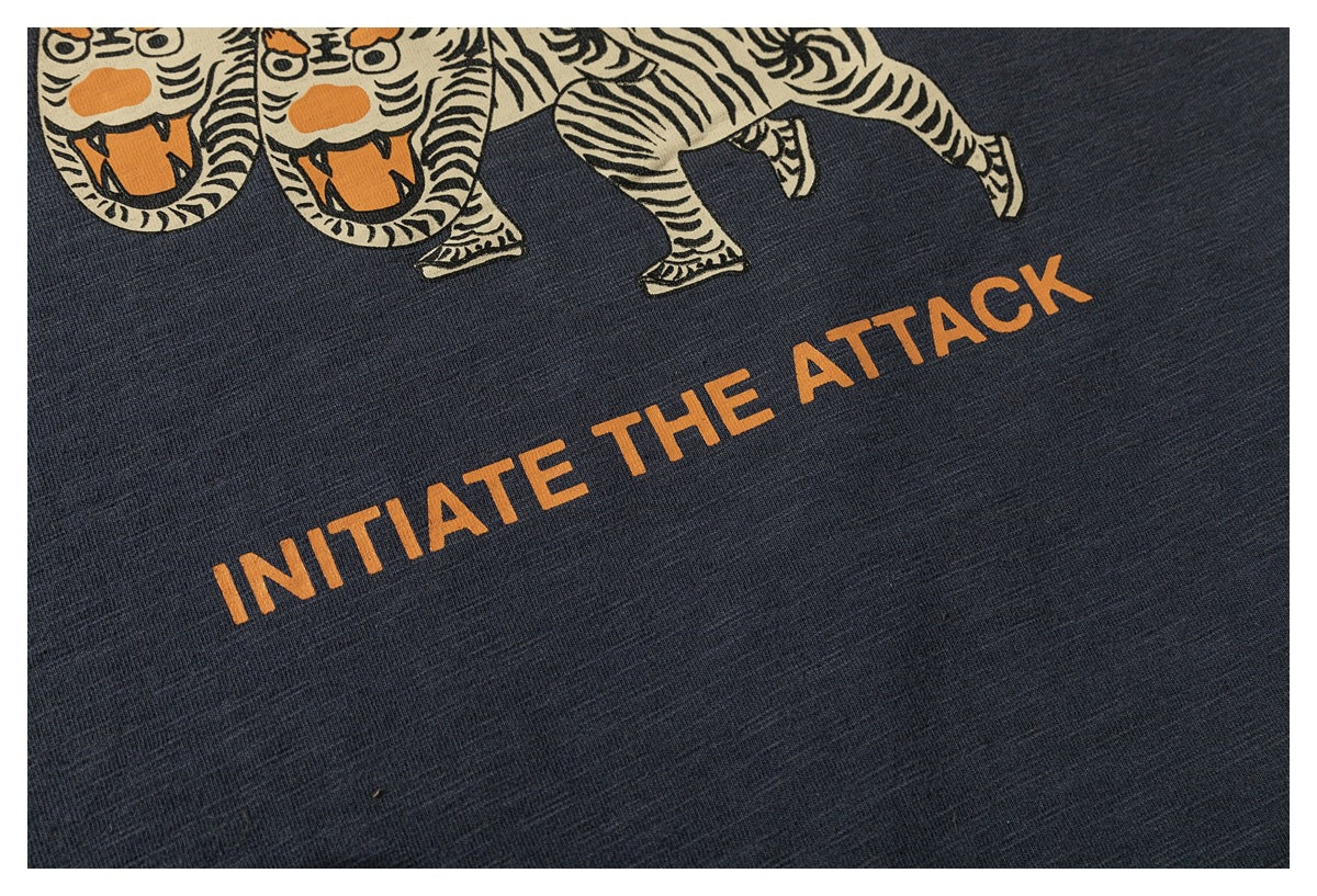 Close-up of the charcoal shirt's orange printed words, “INITIATE THE ATTACK,” beneath part of the graphic.