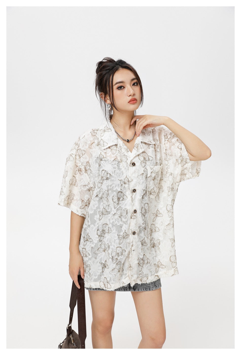 Model wearing an oversized ivory short-sleeve shirt with muted taupe butterfly and floral patterns.