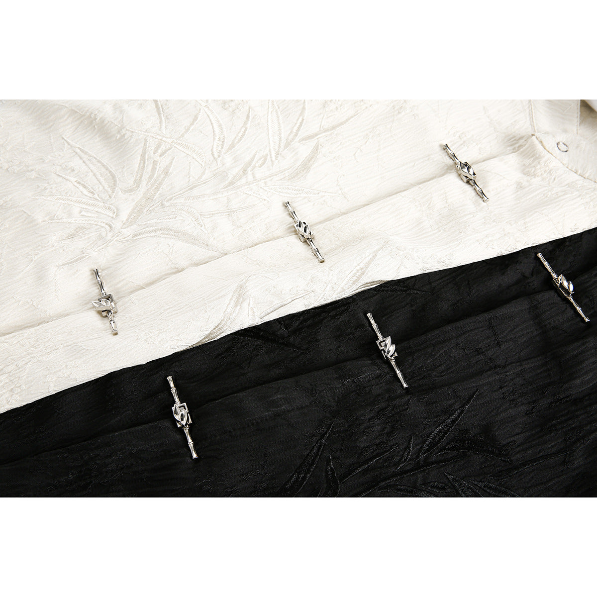 Close-up of ivory and black textured shirt fabric with embroidered designs and silver frog closures.