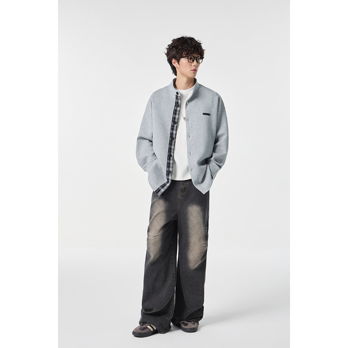 Full-length view of a model wearing a light gray plaid-trim button-front jacket with wide dark jeans.