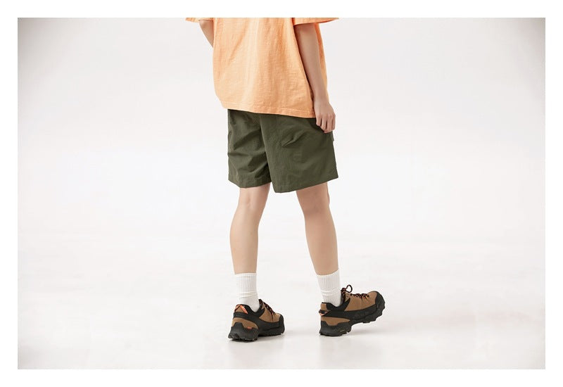 Cropped rear-side view of a person wearing dark olive shorts, a peach T-shirt, white socks and brown hiking shoes.