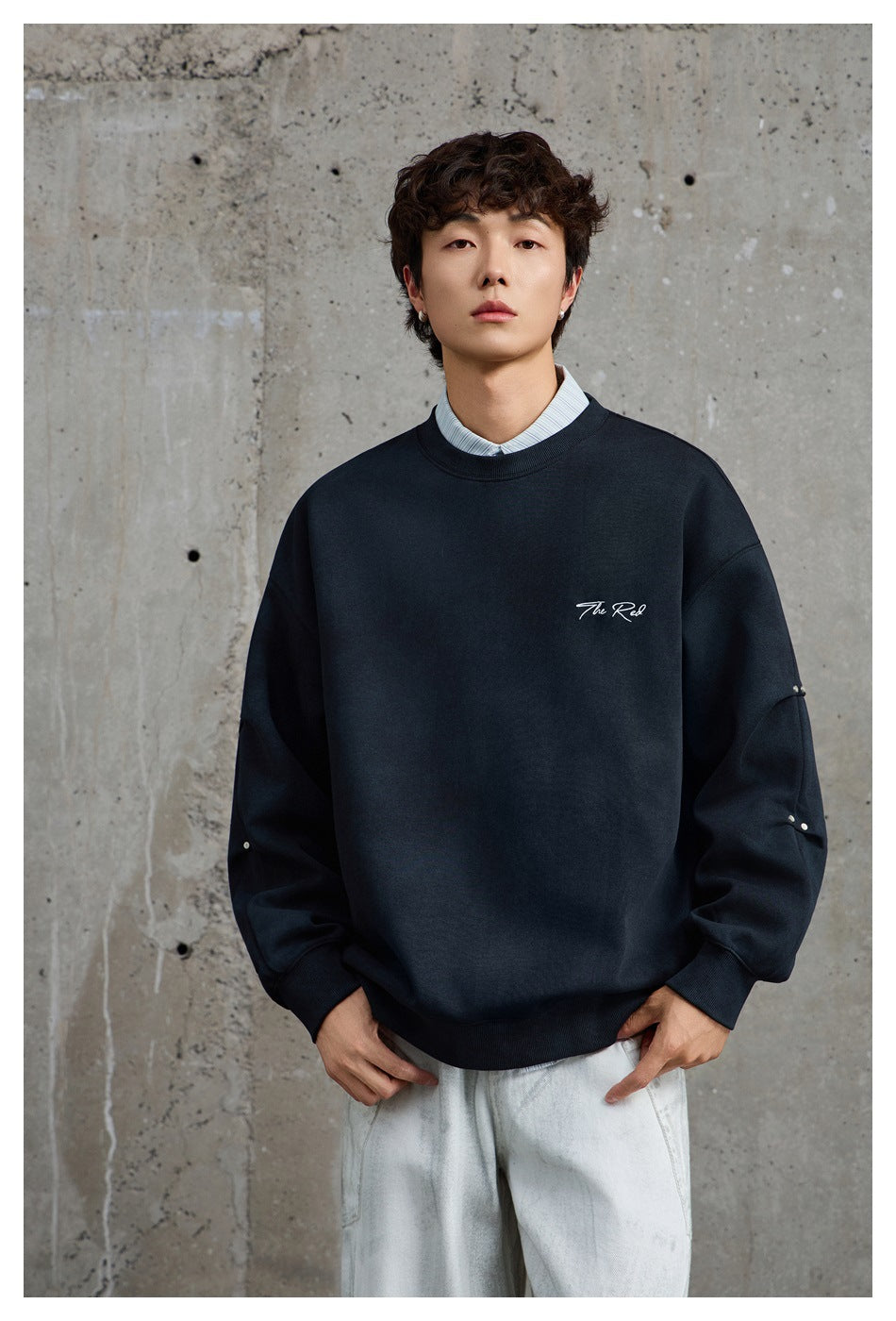 Closer front view of a model wearing a dark navy crewneck sweatshirt with white chest script and studded sleeves.