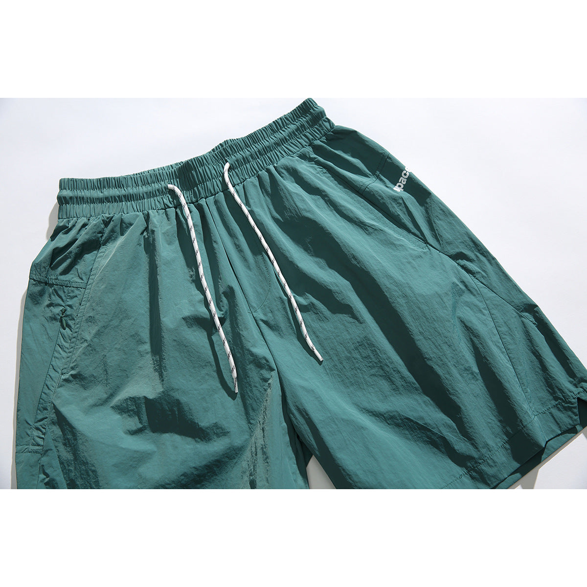 Close-up of teal shorts with an elastic waistband, white drawstrings, and a small white leg logo.