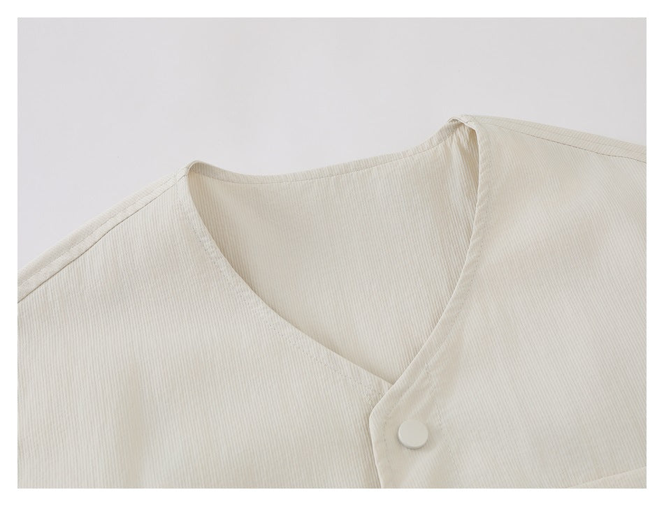 Close-up of an ivory V-neck wrap front with a round snap button and fine vertical texture.