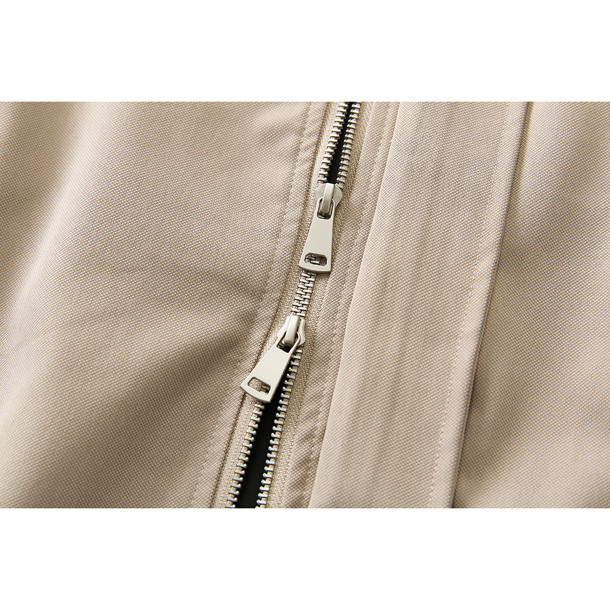 Close-up of two metal zipper pulls on the beige jacket front.