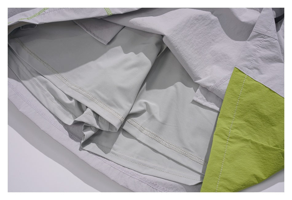 Close-up of overlapping light gray garment panels and stitched seams, with a lime-green section at the edge.