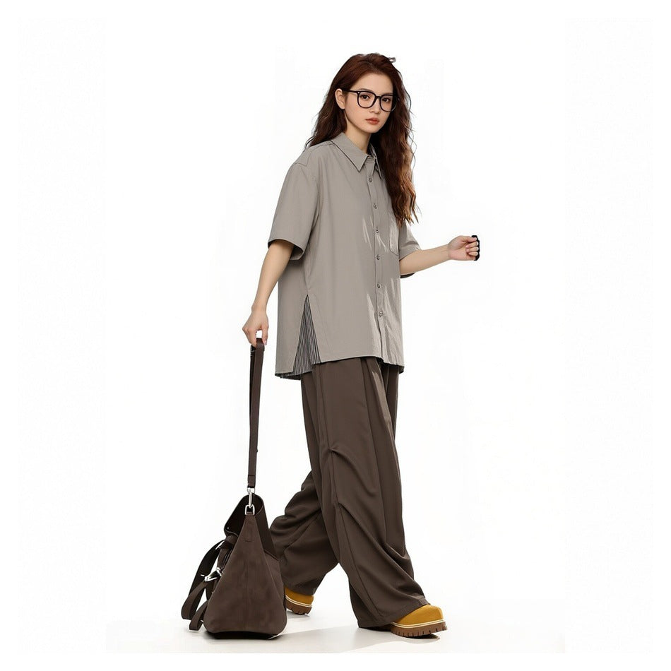 Model wearing a loose taupe short-sleeve button-up shirt with striped side panels and dark brown wide-leg trousers.