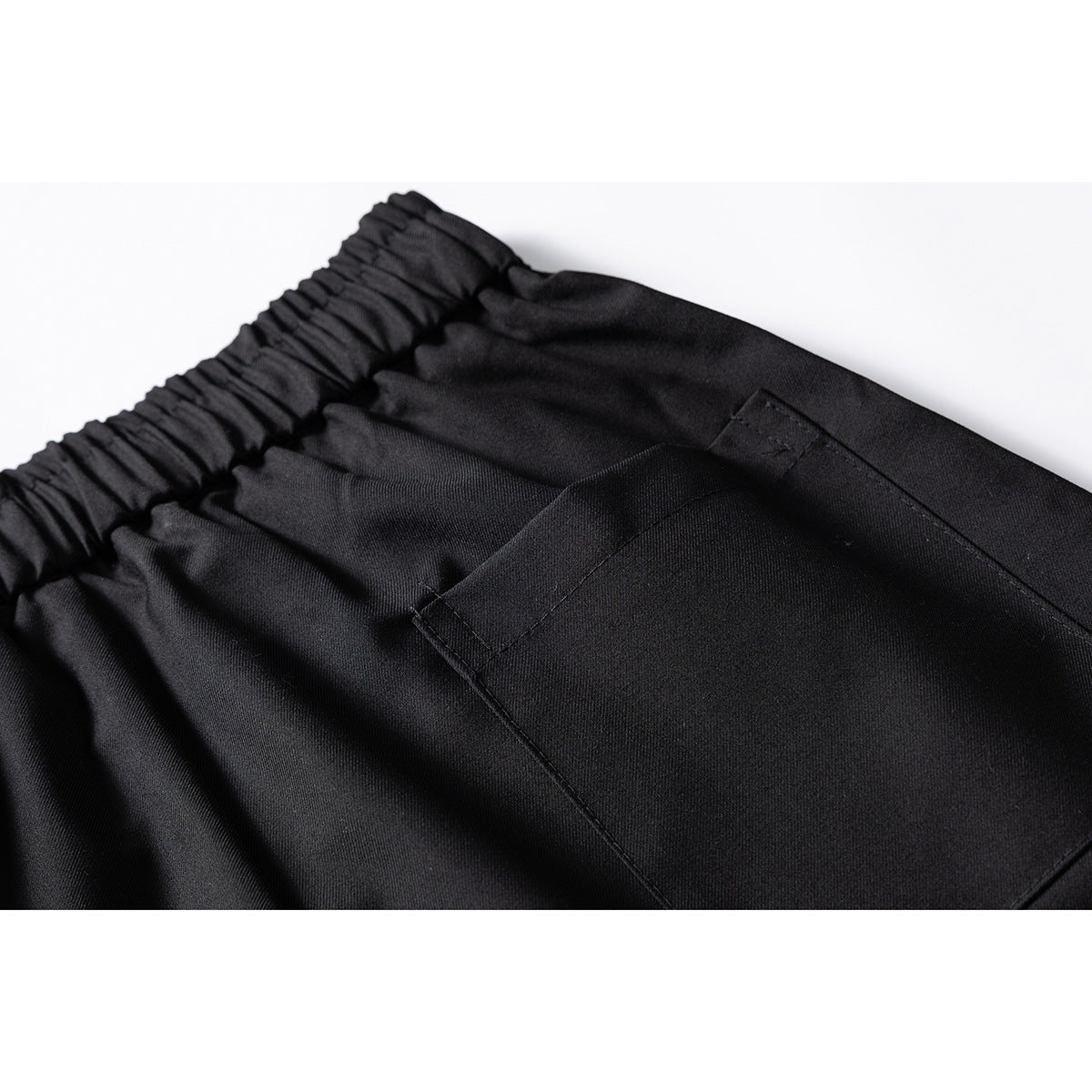 Close-up of black trousers showing the gathered waistband and a large rear patch pocket.