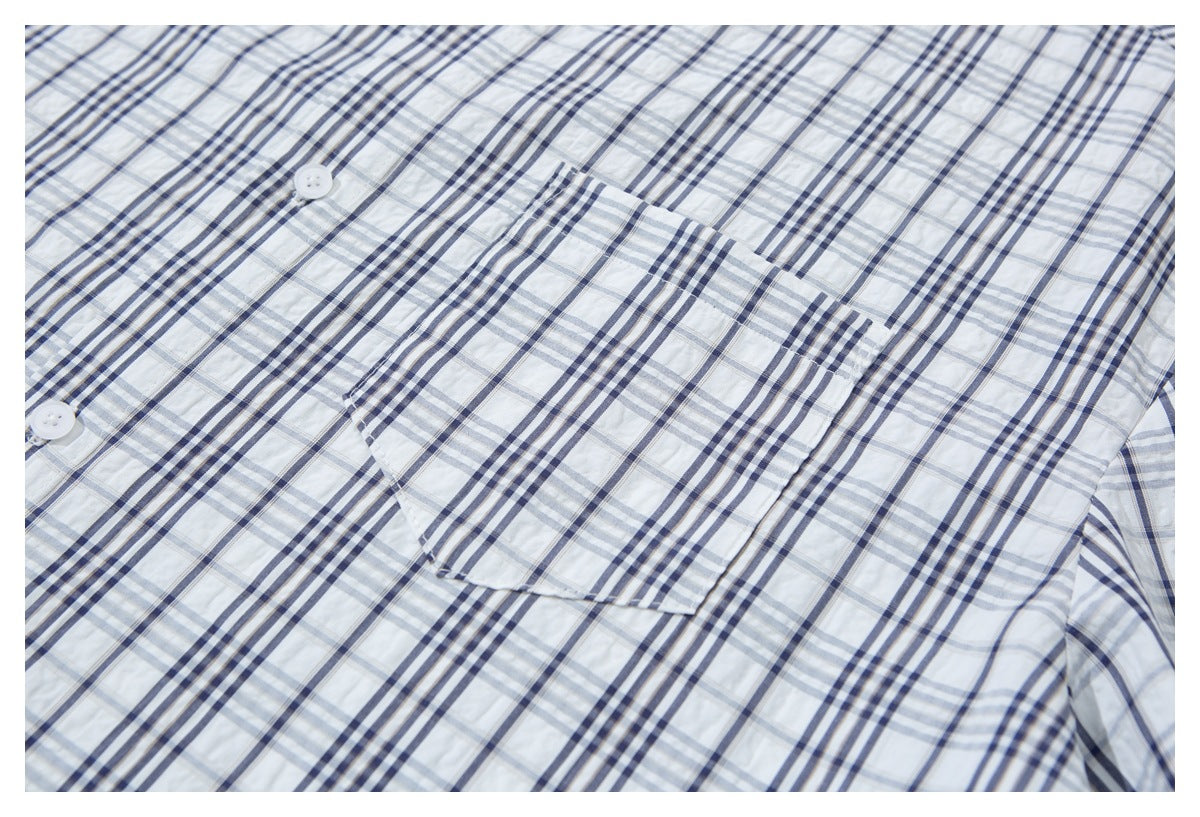 Close-up of a white shirt with navy and gray plaid, showing a button and chest pocket.