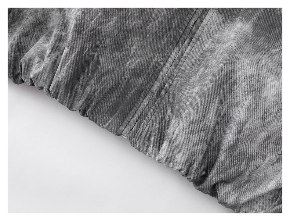 Close-up of the jacket's gathered hem and front seam against gray mottled fabric.