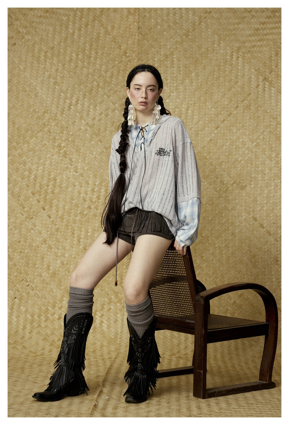 Model wearing a light gray striped hooded top with blue plaid sleeves, lace-up neckline, dark shorts and tall boots.