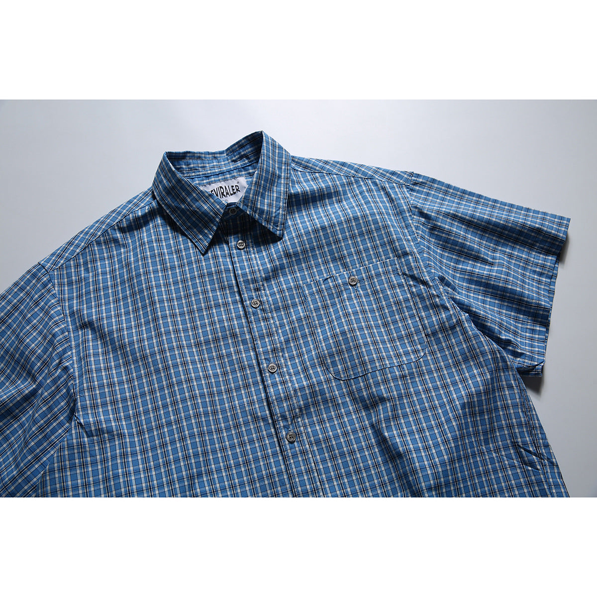 Blue short-sleeve plaid button-up shirt laid flat, with a pointed collar and a buttoned chest pocket.