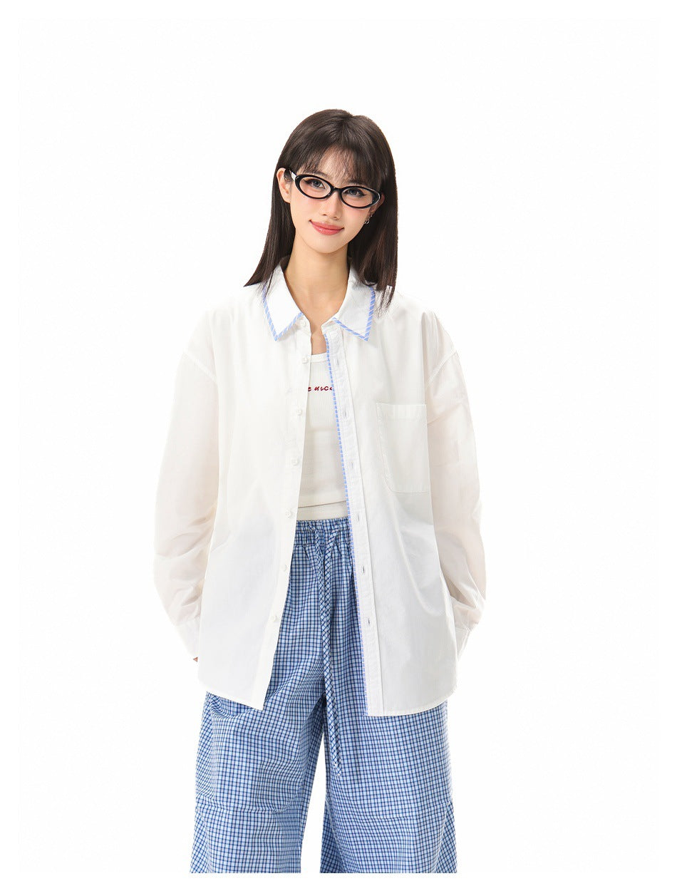 Model wearing a white long-sleeve button-up shirt with blue-trimmed collar and loose blue checked trousers.