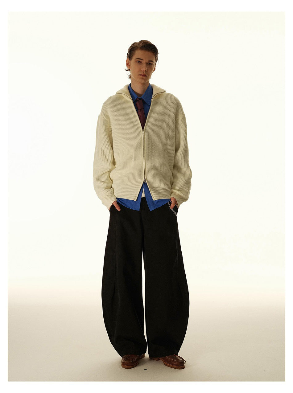 Full-length view of a model in an apricot zip-up knit cardigan, blue shirt, red tie and wide black trousers